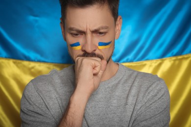 Photo of Sad man with face paint near Ukrainian flag