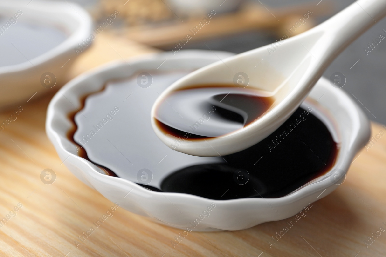 Photo of Spoon with soy sauce over bowl on wooden stand, closeup