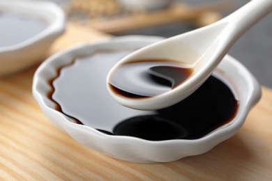 Spoon with soy sauce over bowl on wooden stand, closeup