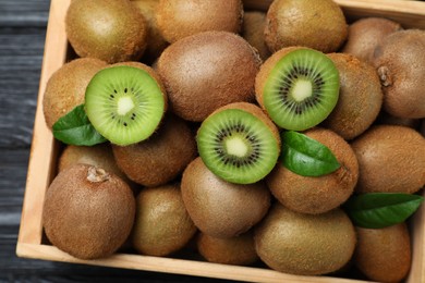Photo of Crate with cut and whole fresh kiwis on black wooden table, top view