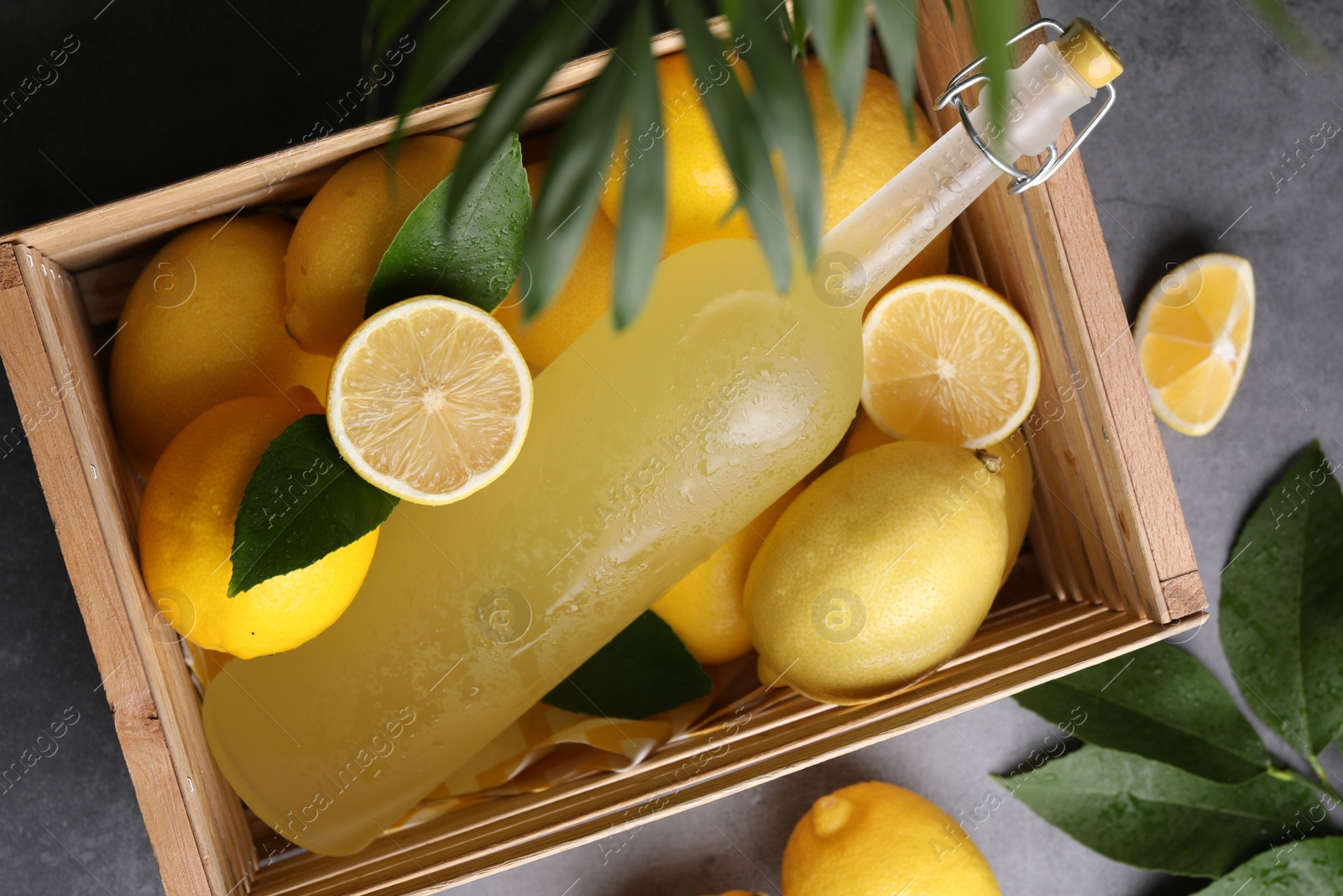 Photo of Tasty limoncello liqueur, lemons and green leaves on grey table, flat lay