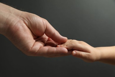 Photo of Father and child holding hands on dark grey background, closeup