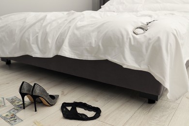Photo of Prostitution concept. High heeled shoes, dollar banknotes and black panties on floor near bed