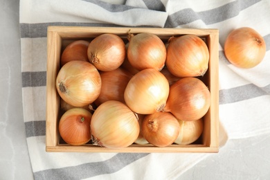 Wooden crate with ripe onions on grey table, flat lay