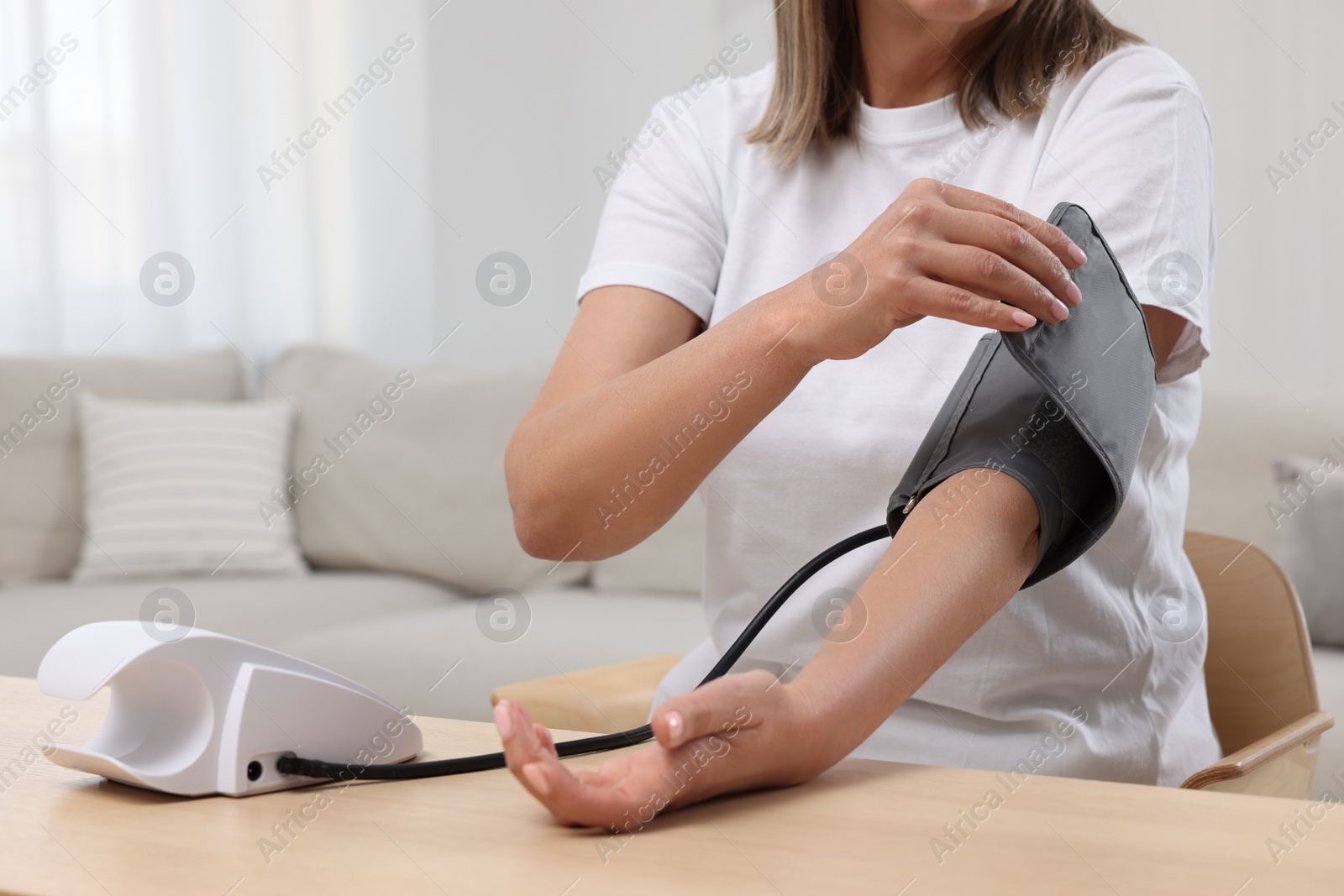 Photo of Woman measuring blood pressure at wooden table in room, closeup