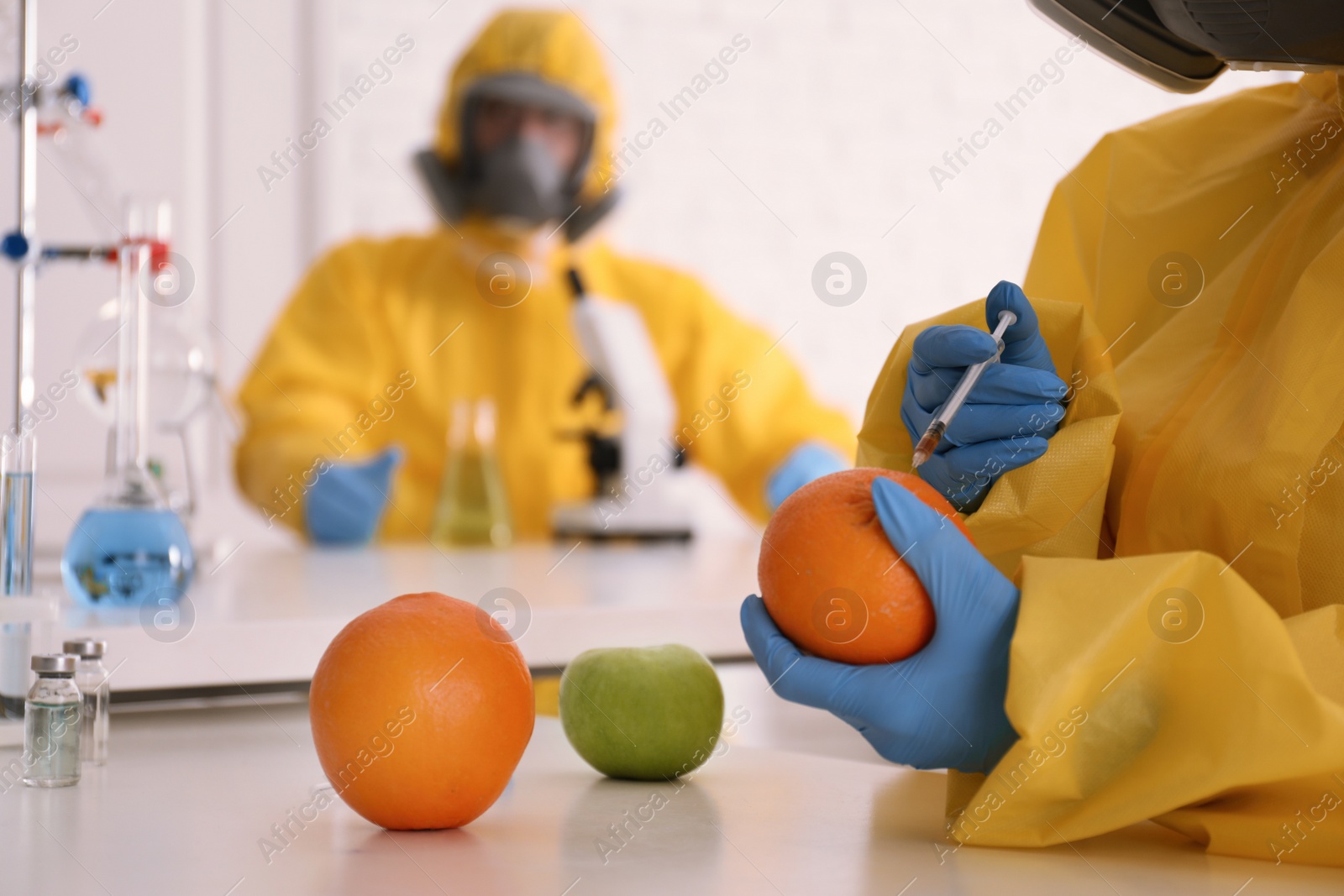 Photo of Scientist in chemical protective suit injecting orange at laboratory, closeup