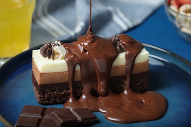 Pouring chocolate onto tasty mousse cake on blue plate, closeup