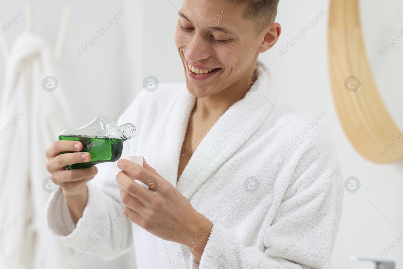 Photo of Young man using mouthwash in bathroom. Oral hygiene