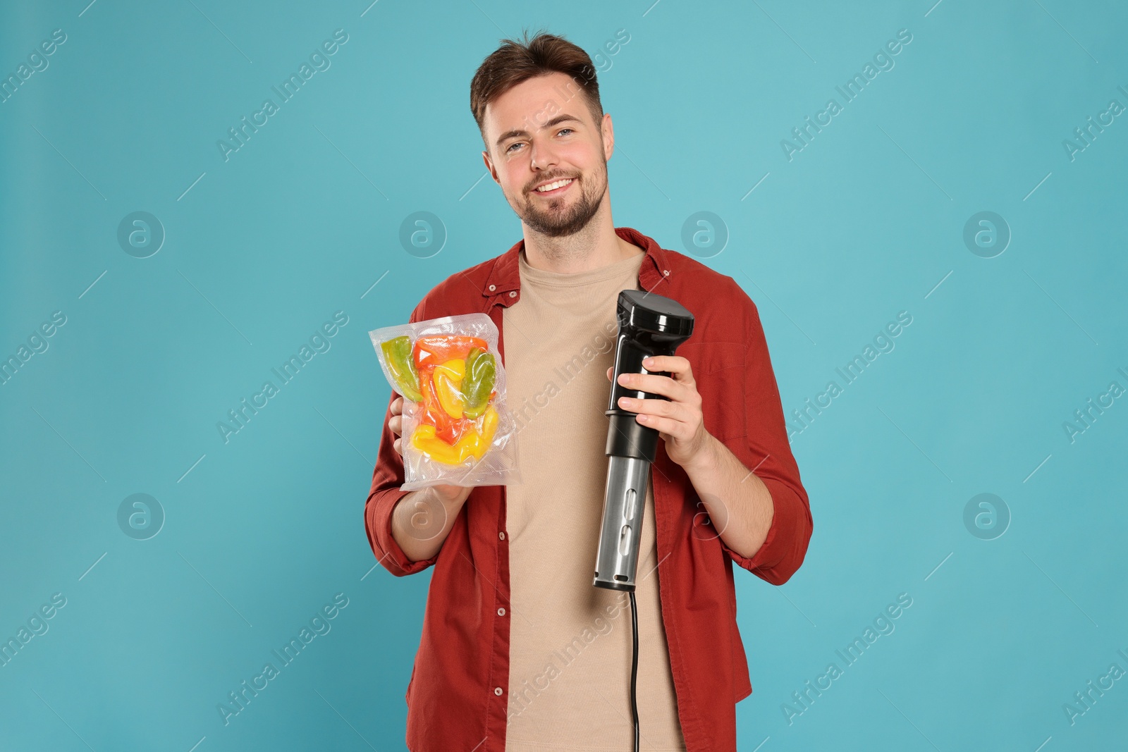 Photo of Smiling man holding sous vide cooker and vegetables in vacuum pack on light blue background