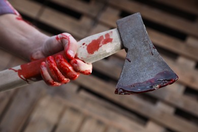 Photo of Man holding bloody axe outdoors, closeup view