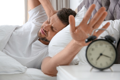 Sleepy man turning off alarm clock at home in morning