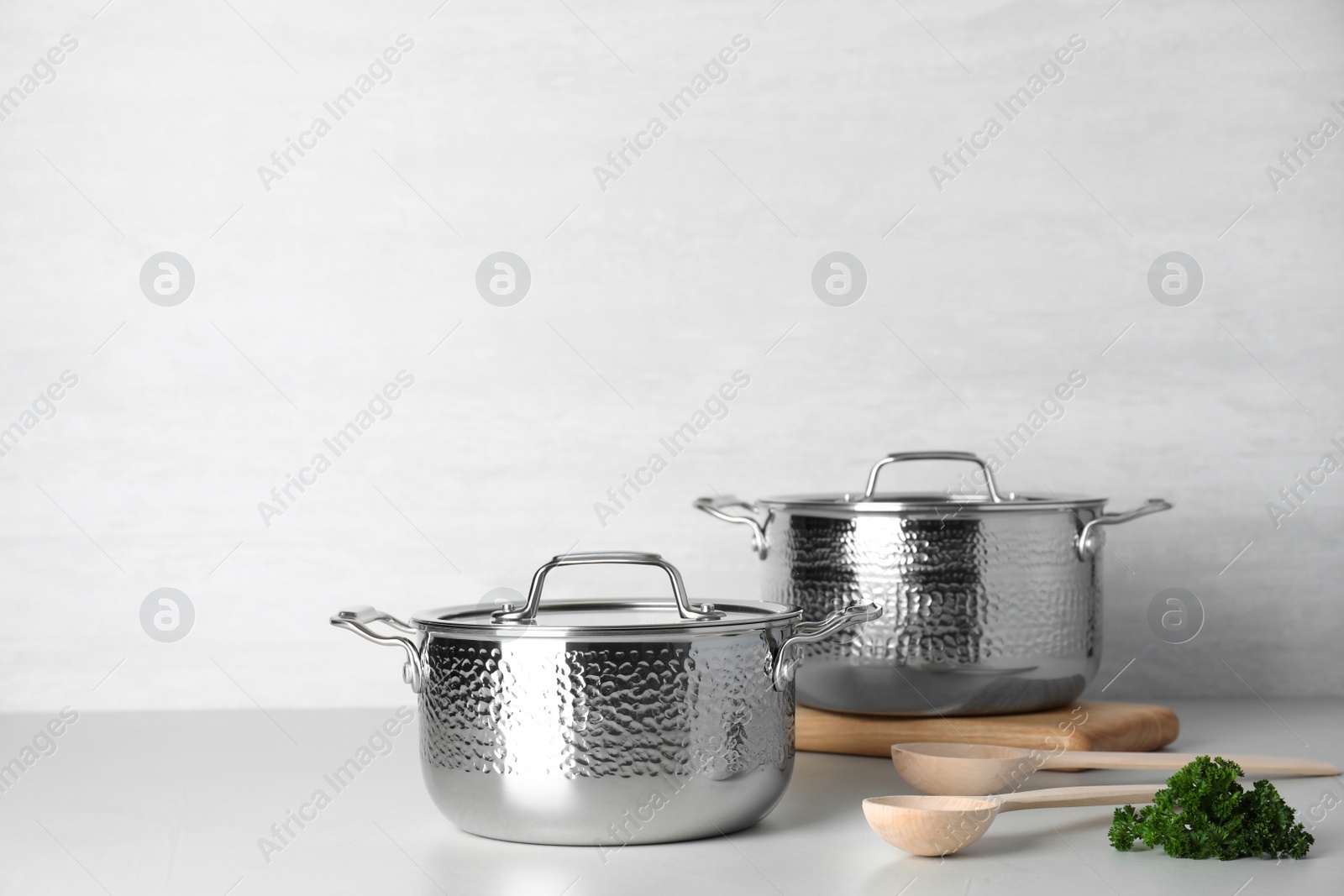 Photo of Clean saucepans and spoons on table against light background. Space for text