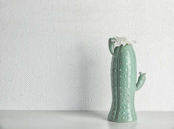 Trendy cactus shaped vase with flower on table against light wall. Creative decor