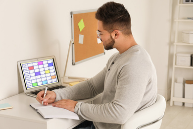 Photo of Young man using calendar app on laptop in office