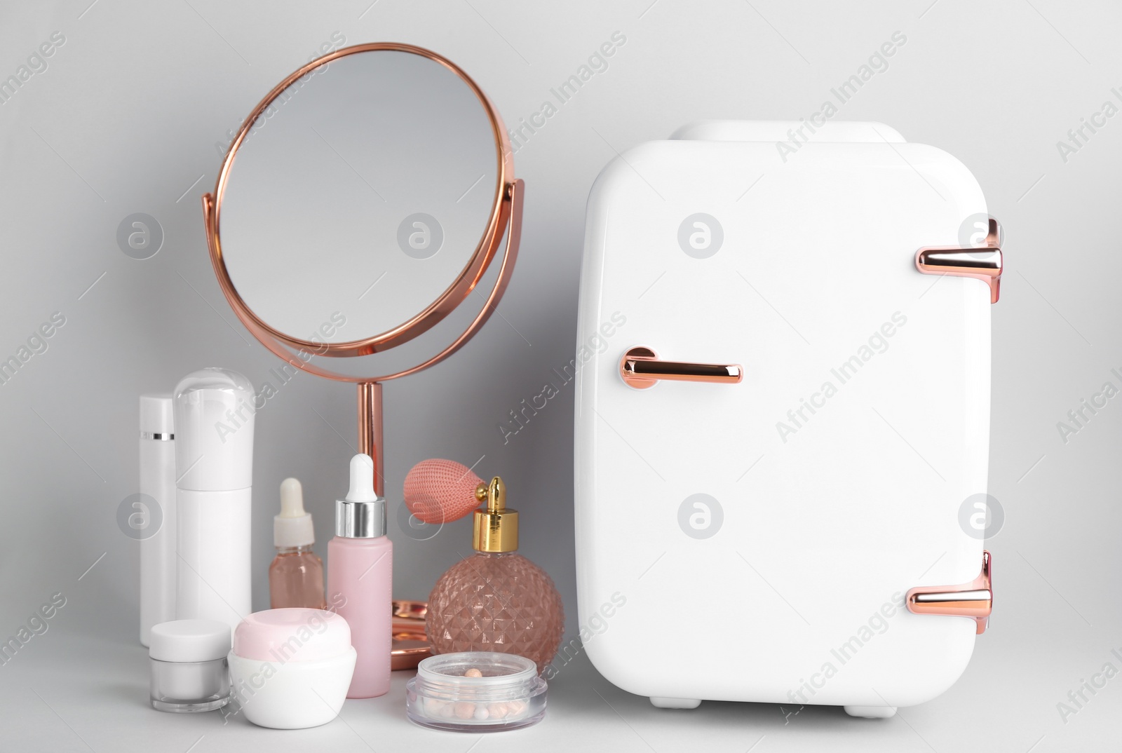 Photo of Cosmetic refrigerator and skin care products on light background