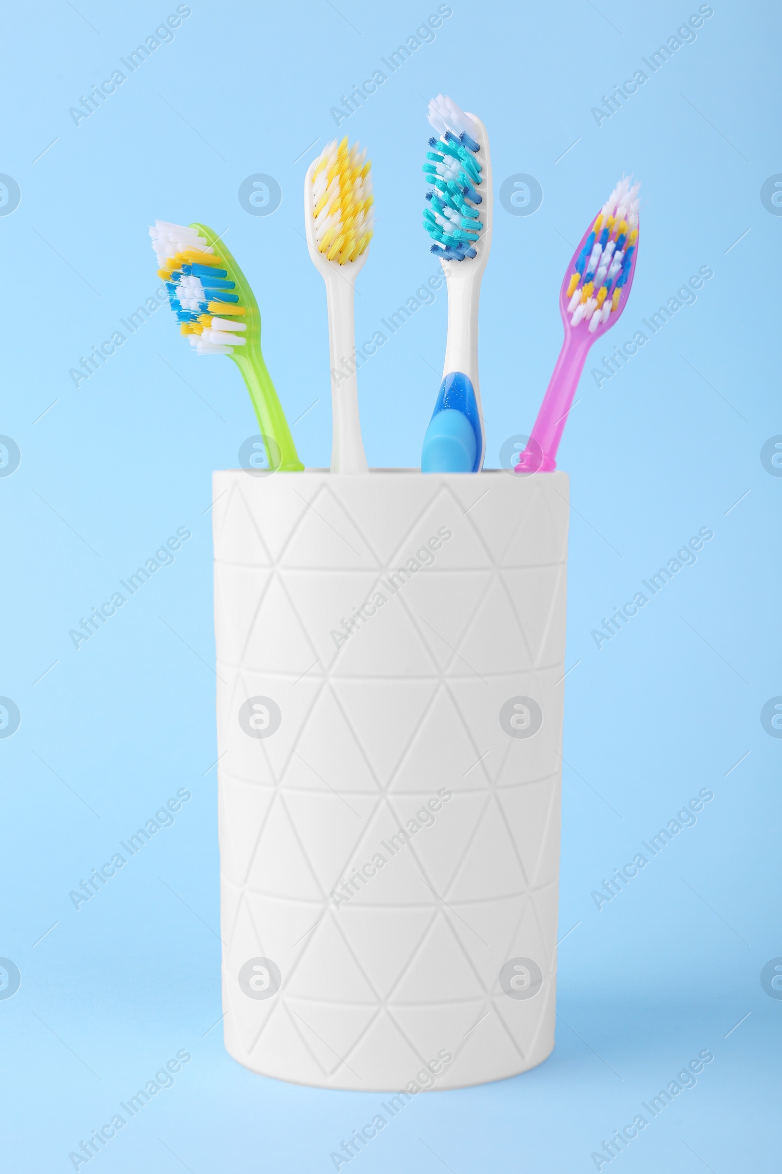 Photo of Different toothbrushes in holder on light blue background