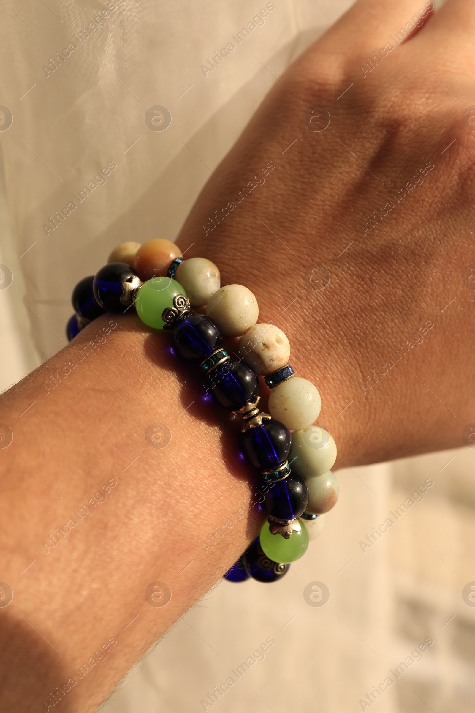 Photo of Woman wearing beautiful bracelets with gemstones on blurred background, closeup