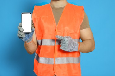 Photo of Man in reflective uniform showing smartphone on light blue background, closeup