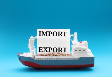 Photo of Toy cargo vessel with words Import and Export on light blue background