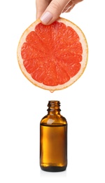 Woman holding slice of grapefruit above bottle with essential oil on white background