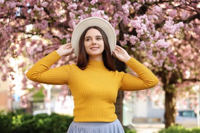 Beautiful woman in hat near blossoming tree on spring day