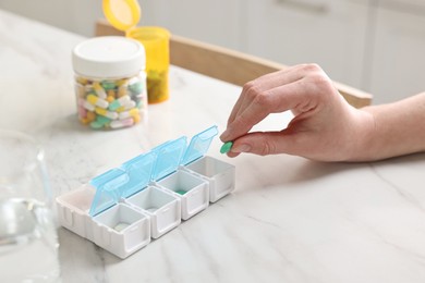 Woman with pills, organizer and glass of water at white marble table, closeup