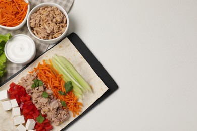 Photo of Delicious tortilla with tuna and vegetables on white table, flat lay. Cooking shawarma
