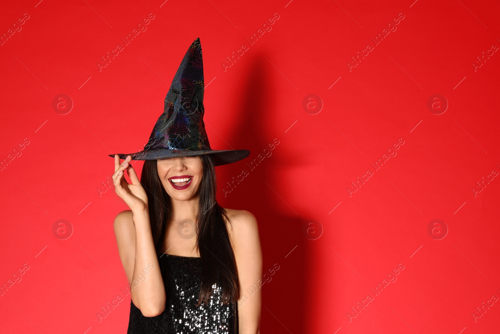 Photo of Beautiful young woman wearing witch costume for Halloween party on red background, space for text