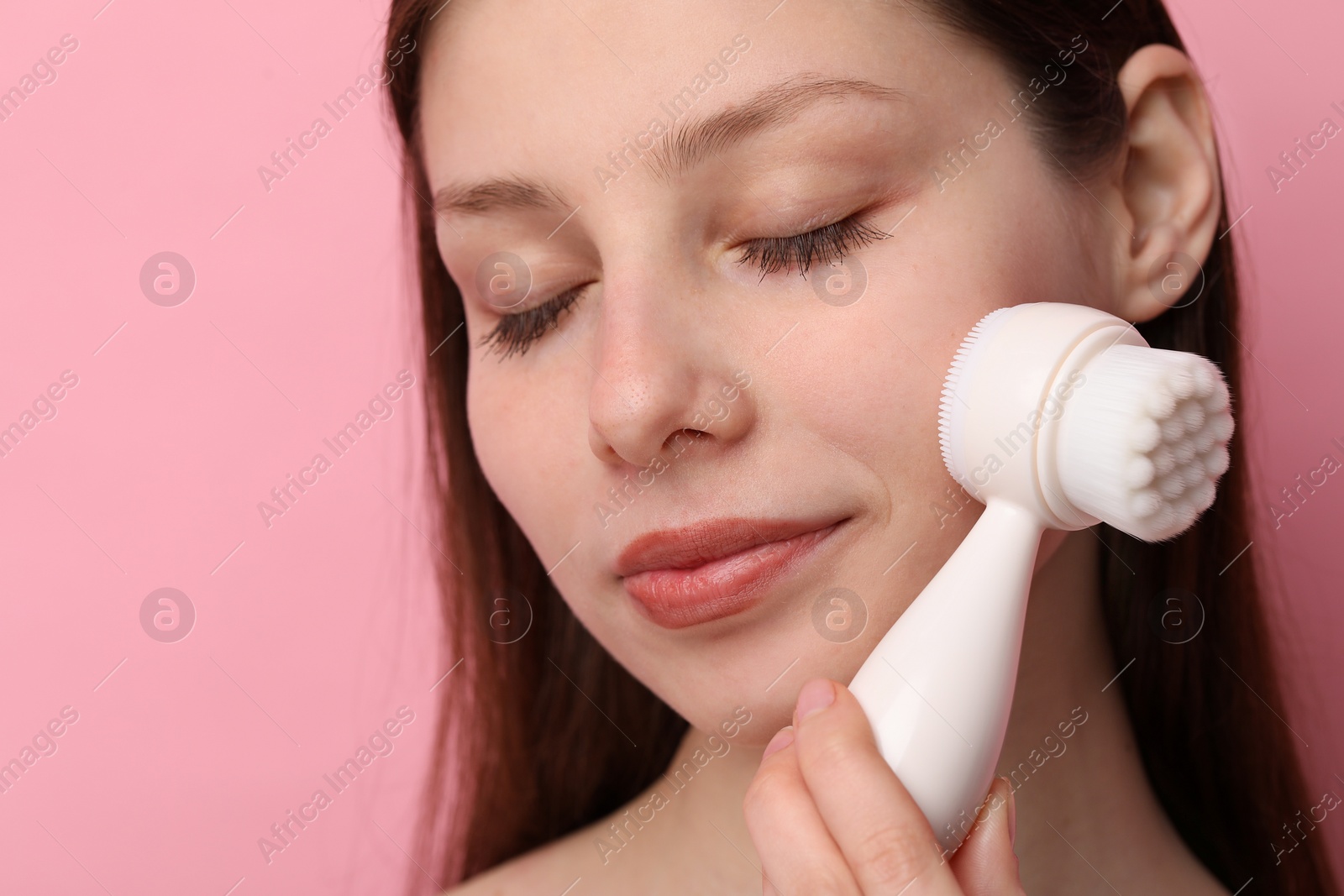 Photo of Washing face. Young woman with cleansing brush on pink background, closeup