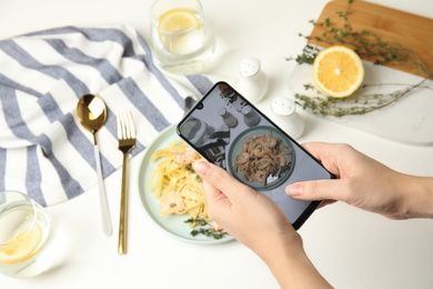 Photo of Food blogger taking picture of tasty pasta with shrimps and tomatoes at light table, closeup