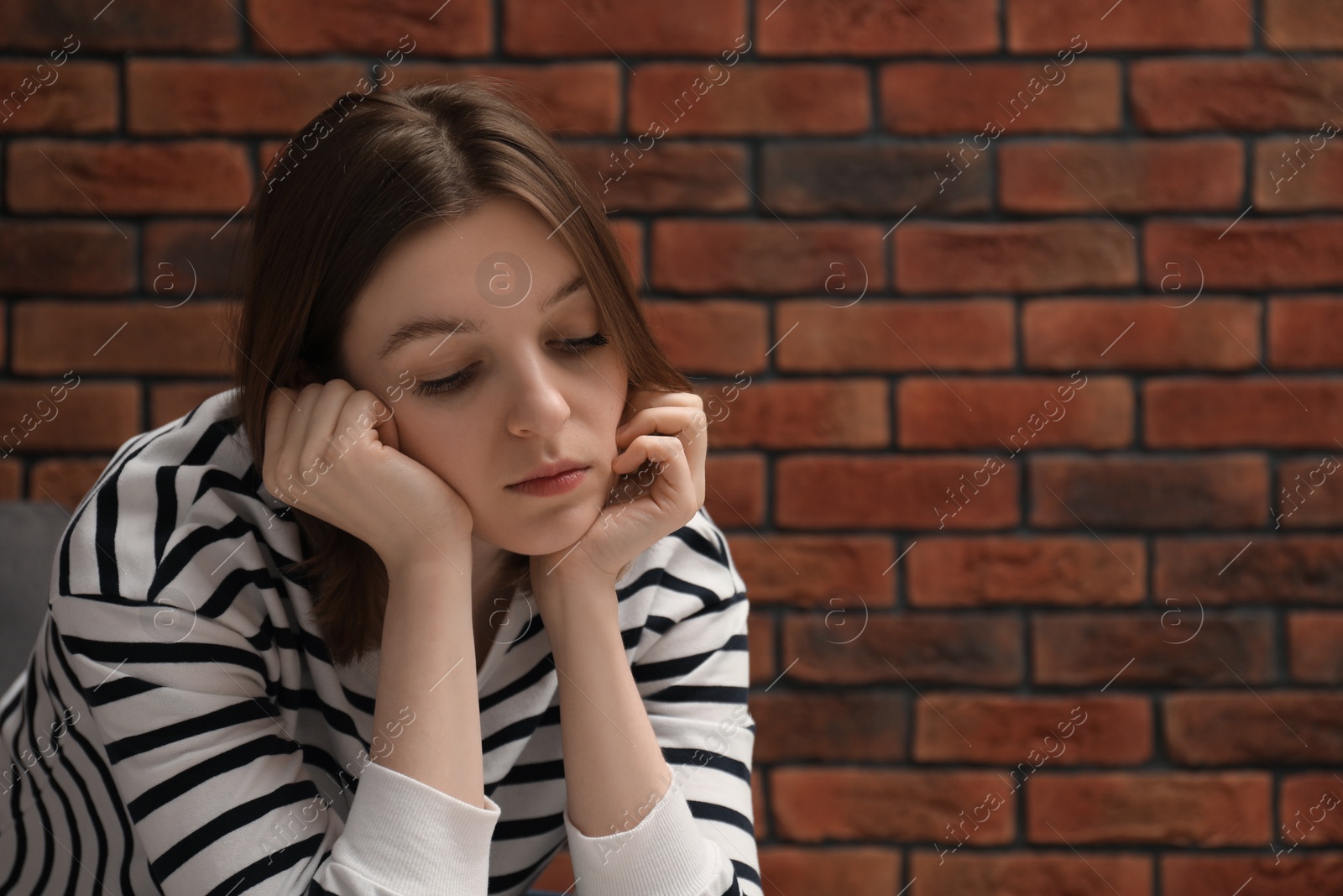 Photo of Sad young woman near brick wall, space for text