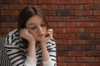 Photo of Sad young woman near brick wall, space for text