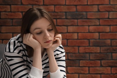 Sad young woman near brick wall, space for text