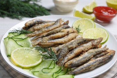 Photo of Plate with delicious fried anchovies, lime and cucumber on table, closeup
