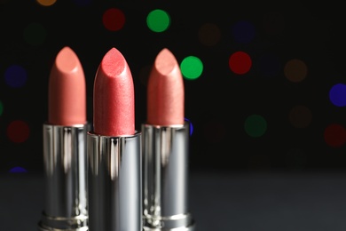 Photo of Different lipsticks on table against blurred lights. Space for text