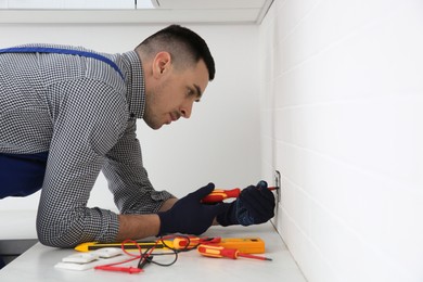 Electrician with screwdriver repairing power socket indoors