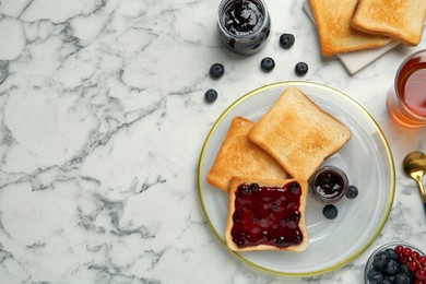 Delicious toasts served with jam, tea and berries on white marble table, flat lay. Space for text