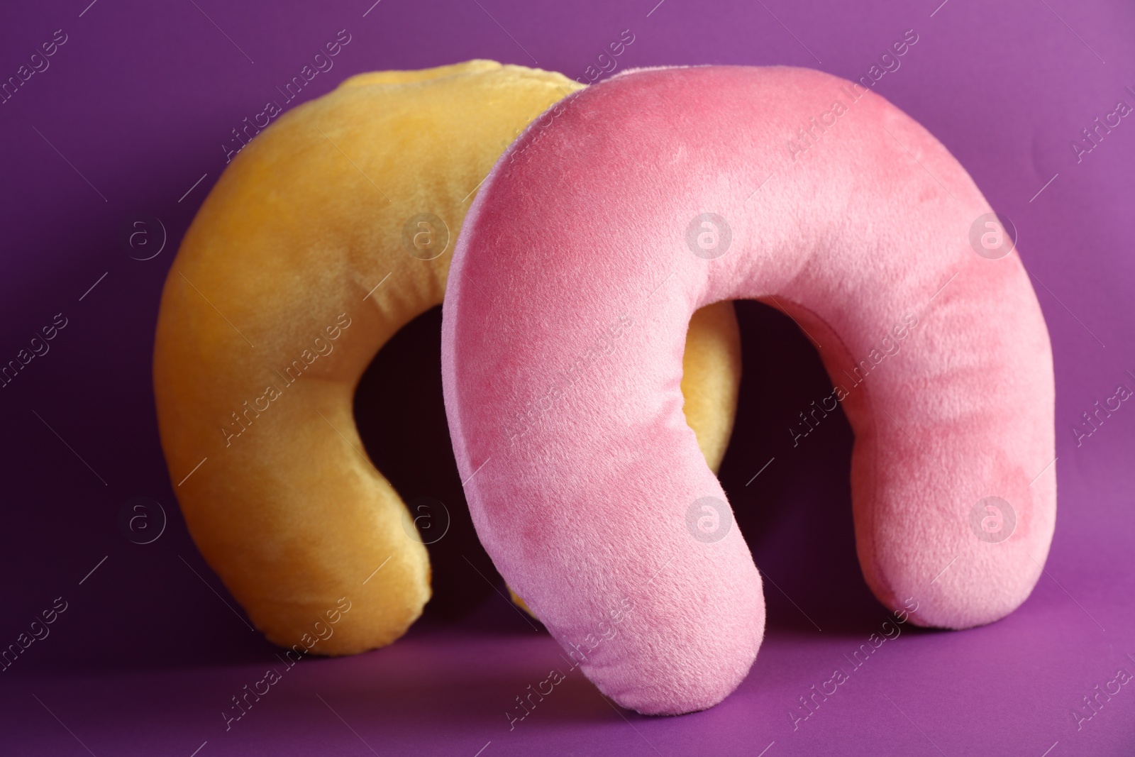 Photo of Pink and yellow travel pillows on violet background