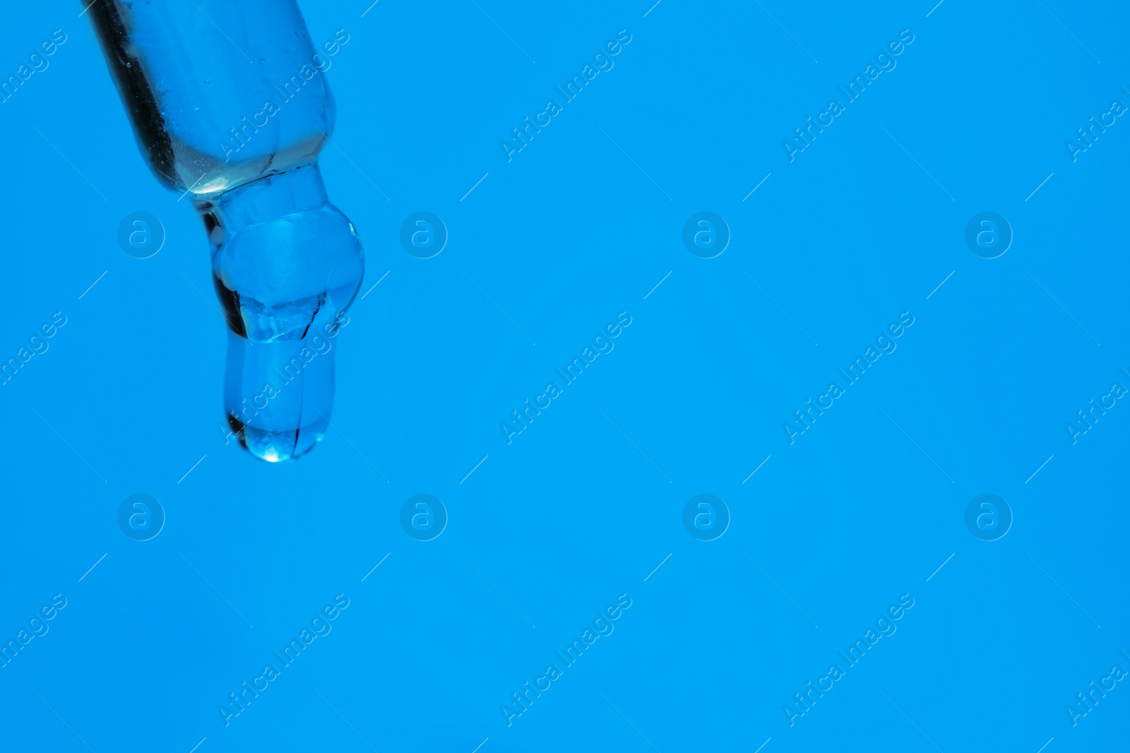 Photo of Dripping face serum from pipette on blue background, closeup. Space for text