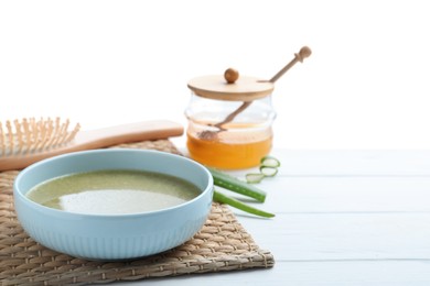 Photo of Homemade hair mask in bowl, fresh ingredients and brush on wooden table against white background. Space for text