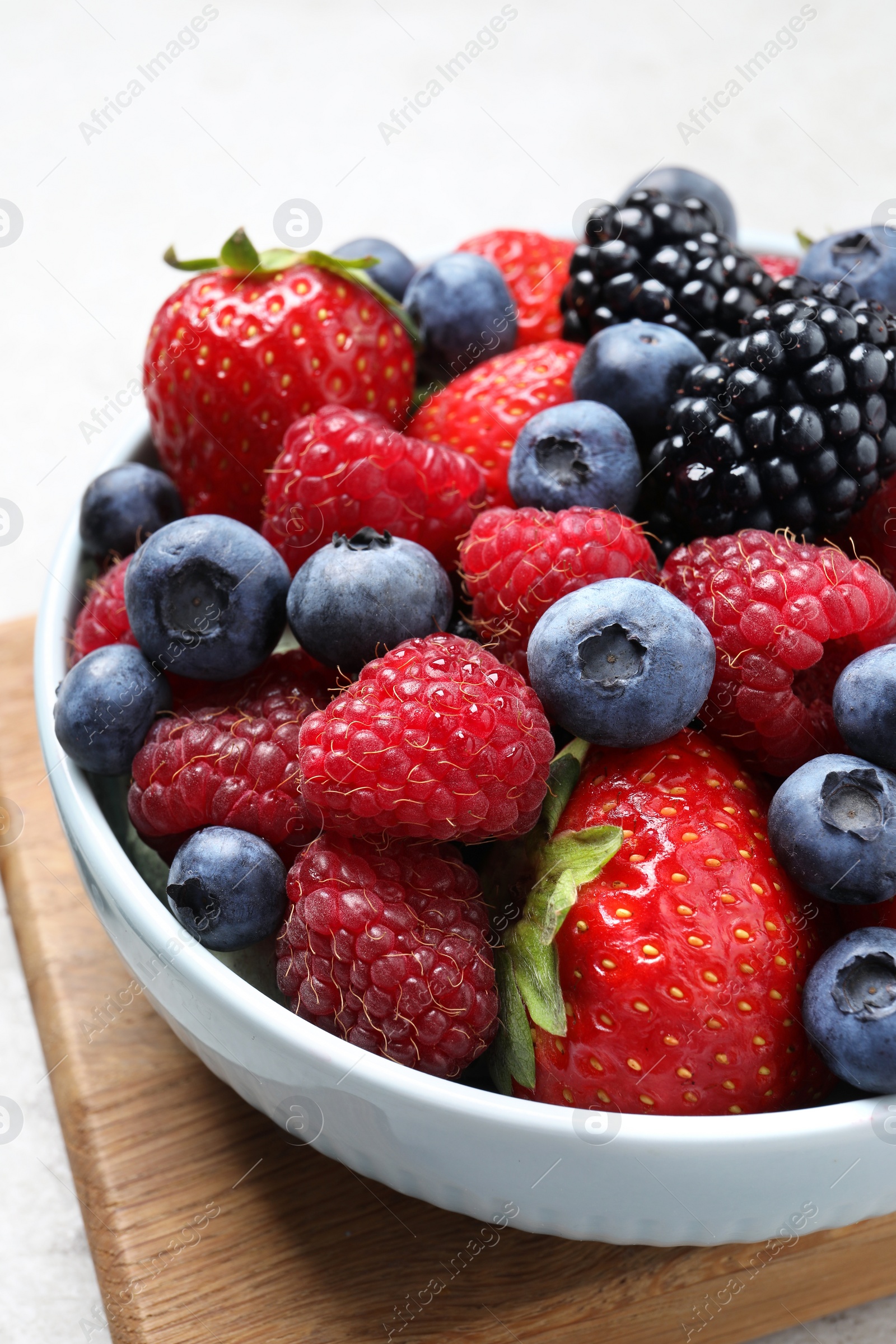 Photo of Many different fresh ripe berries in bowl on light grey table, closeup