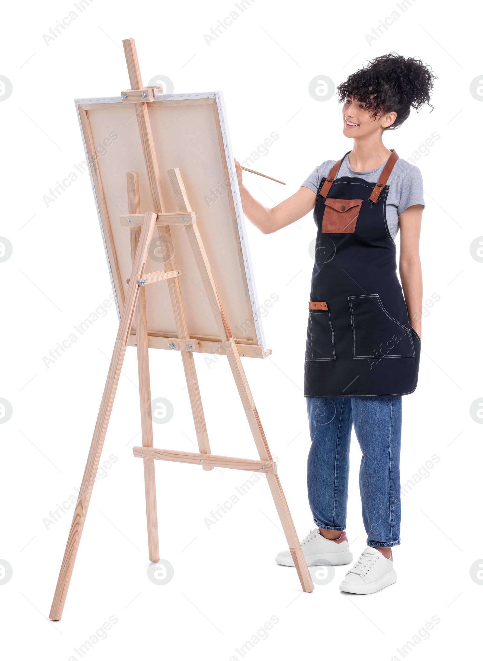 Photo of Young woman painting on easel with canvas against white background