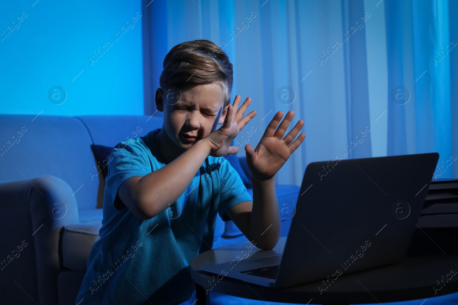Photo of Frightened little child with laptop in dark room. Danger of internet