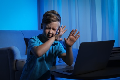 Photo of Frightened little child with laptop in dark room. Danger of internet