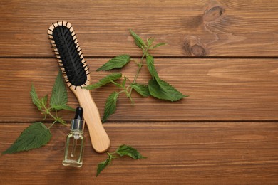 Photo of Stinging nettle extract, leaves and brush on wooden background, flat lay with space for text. Natural hair care
