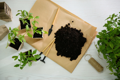 Photo of Flat lay composition with tomato seedlings, gardening tools and soil on white wooden table