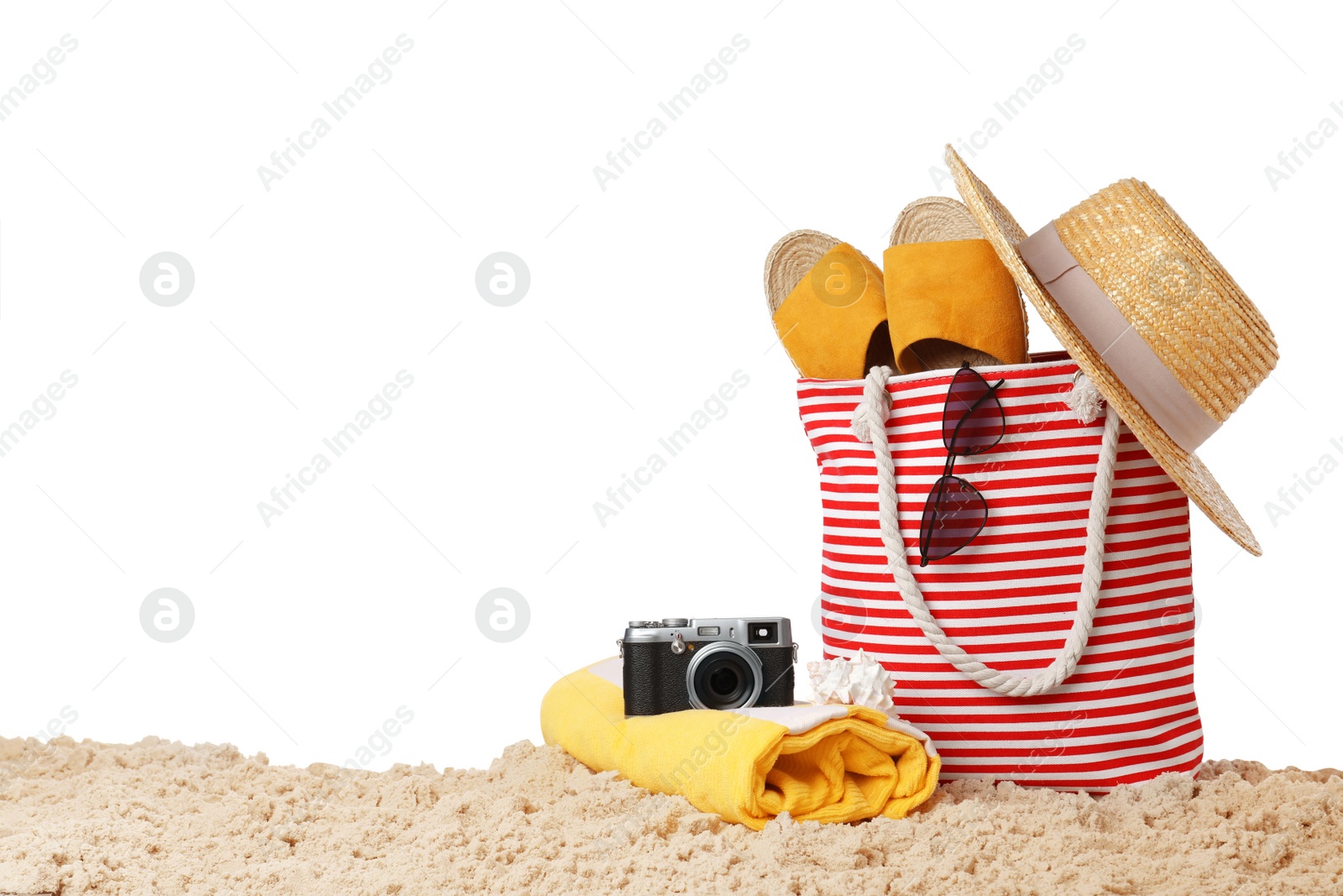 Photo of Stylish bag with beach accessories and camera on sand against white background