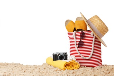 Stylish bag with beach accessories and camera on sand against white background