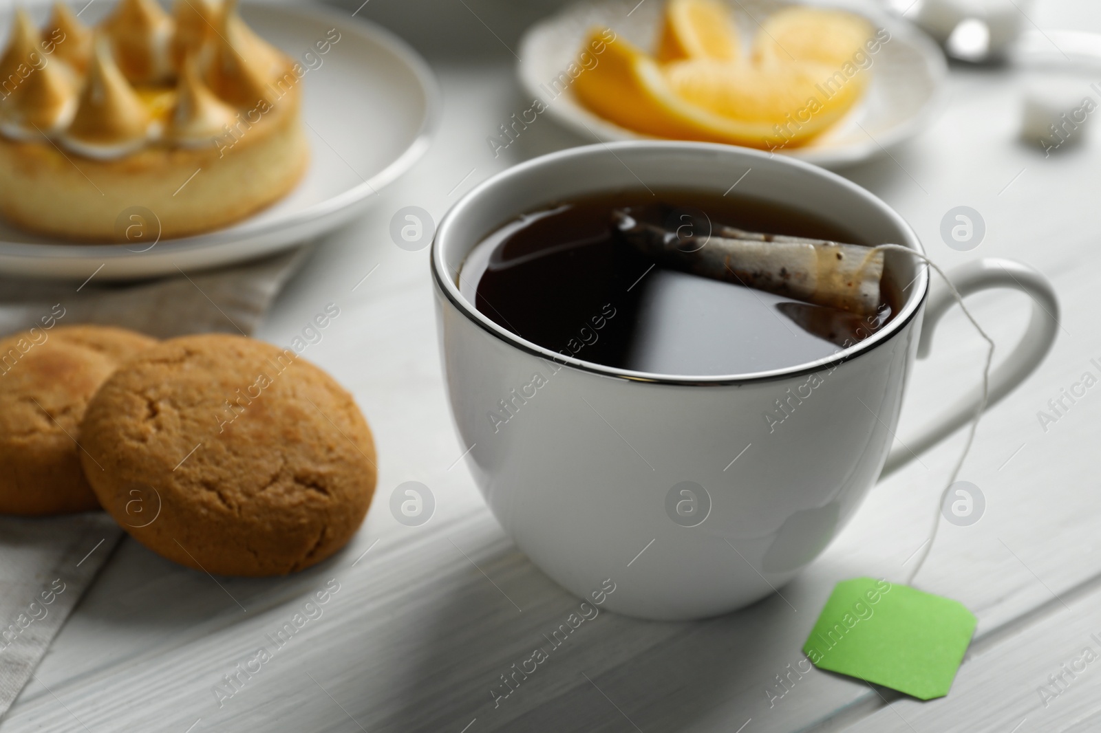 Photo of Tea bag in cup of hot water and cookies on white wooden table