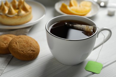 Photo of Tea bag in cup of hot water and cookies on white wooden table